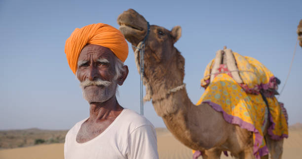 istock Indian man posing with camels on sand dunes, Rajasthan, India 1957403234