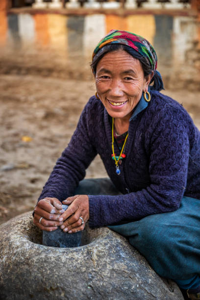 Tibetan woman using a stone mortar to make flour, small village in Upper Mustang. Mustang region is the former Kingdom of Lo and now part of Nepal,  in the north-central part of that country, bordering the People's Republic of China on the Tibetan plateau between the Nepalese provinces of Dolpo and Manang.