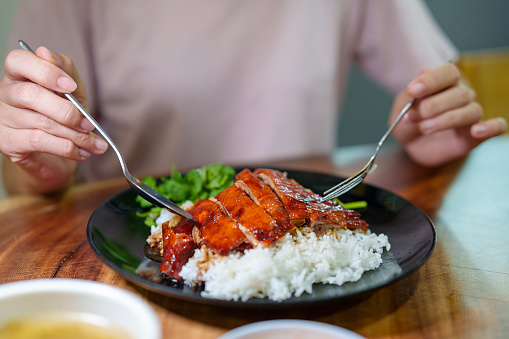 In a close-up view, a young Asian woman enjoying a plate of Asian-style Roasted Duck over Rice.