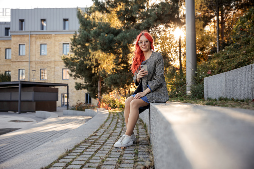 Young red haired business confident  woman using smart phone outdoor of the city sunset background.