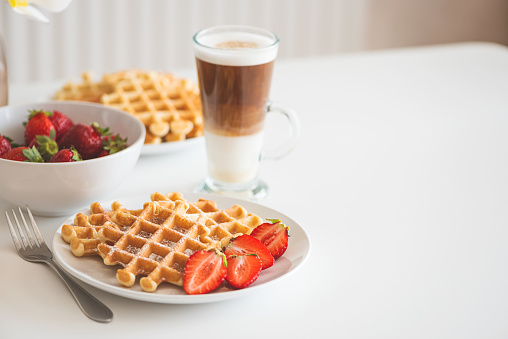 Belgian waffles with strawberry and coffee latte on white plate. Breakfast food concept. Copy space