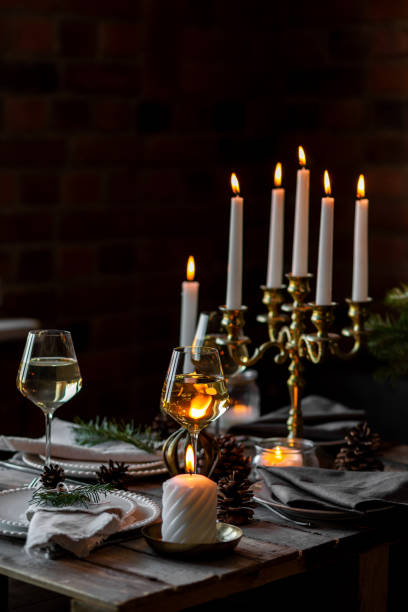 istock Beautiful table setting for family Christmas dinner at home. Cozy atmosphere, candlelight. Wine glasses, vintage chandelier, elegant interior. Fir tree branches, wooden furniture, dark, bokeh 1957435152