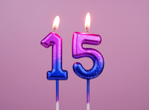 Pink and blue birthday candles burning on pink background. Number 15.