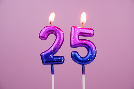 Pink and blue birthday candles burning on pink background. Number 25.