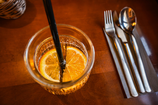 Fruity drink with sliced orange in glass with straw, cutlery. Closeup on restaurant table, top view.
