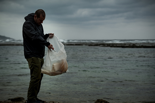 A man visiting the ocean in Okinawa notices plastic trash on the beach and starts to clean it up alone.