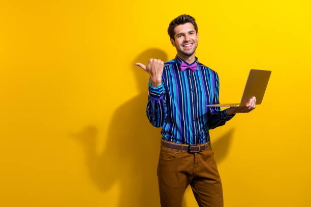 istock Portrait of smart guy dressed shirt bow tie hold laptop indicating at offer empty space isolated on vibrant yellow color background 1957466940