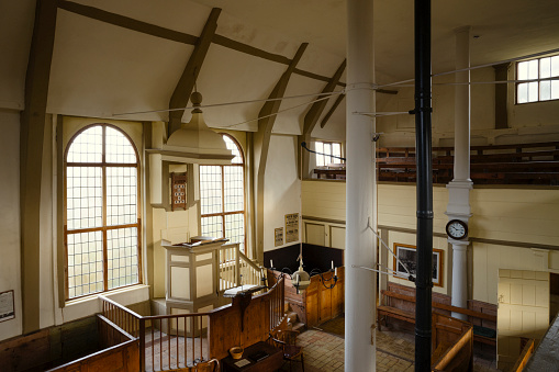 Elevated view of the interior of Walpole Old Chapel, with pulpit, pews, chairs, windows with natural light.
