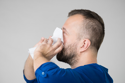 Man having flu, sneezing into hygienic tissue. Guy being sick, allergic blowing his nose.