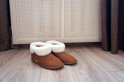 Brown ugg boots with white fur. Home slippers near the battery in the room.