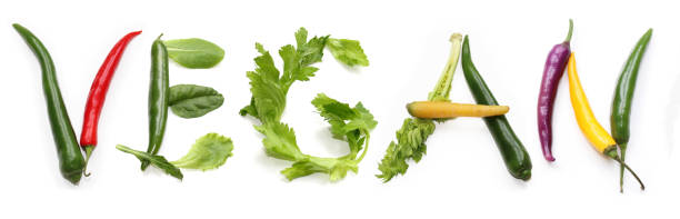 letters V E G A N from red, green, purple, yellow chili pepper, salad lettuce leaf letters, bowl