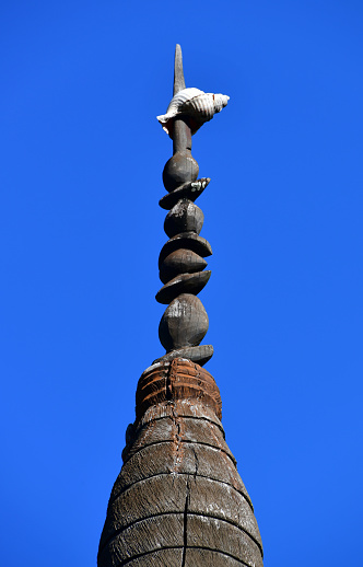 Nouméa, South Province, New Caledonia: a 'fleche faitiére' (rooftop arrow) at the center of Mwaka Square, Maréchal Foch Avenue, downtown Nouméa - an indigenous Melanesian symbol that came to represent the Kanak people and the independence movement (FLNKS).  A respected emblem of the Kanak chiefdom, the 'fleche faitiére', is a traditional element of Kanak architecture, which dominates and adorns the cone-shaped thatched roof of the large huts and ceremonial totems of a clan. It is made with houp (Montrouziera cauliflora), a rot-proof wood from high-altitude forests and has a a calling conch at the top.