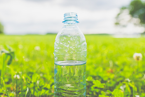 Plastic Bottle with fresh transparent water on green grass on sunny summer day.Nature texture, green blurred background, wallpaper.