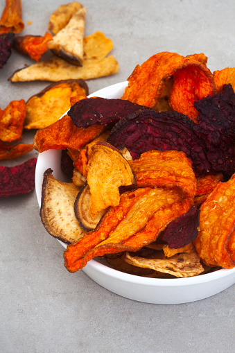 Crisps made of root vegetables. Carrots, beetroot, and sweet potato. On mottled grey surface with copy space
