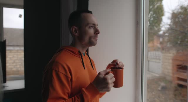 Man drinking tea standing in home near window