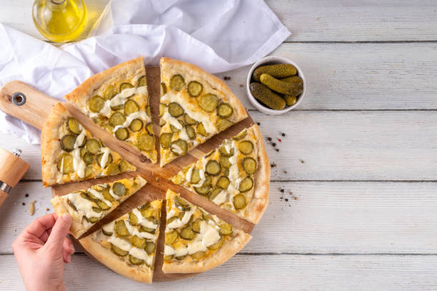 Pickle Pizza with cheese sauce and pickled cucumber Pickle Pizza with cheese sauce and pickled cucumbers. Trendy asian style, vegan sour taste pizza on kitchen table copy space dill pickle stock pictures, royalty-free photos & images