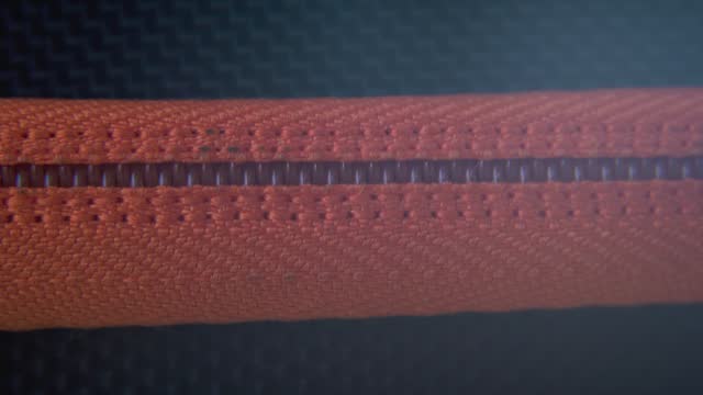 A cinematic macro close-up shot of a hard case zipper being closed, orange rexture, metal zip, black box, photography gear, professional studio lighting, static 4K video