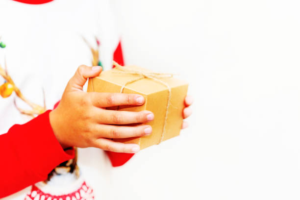 Young boy hands in pullover holding Christmas gift box on gray background.Christmas and New Year banner.Copy space.