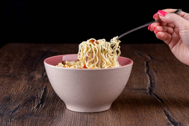 istock A woman's hand holds a fork with ready-made instant noodles. 1957700529