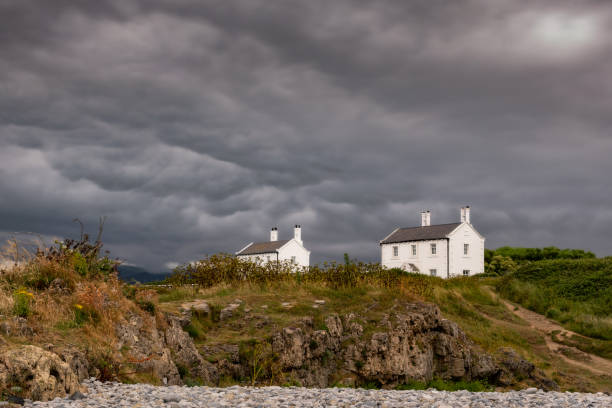 Stunning white cottage near a beach under dramatic storm clouds - Former lighthouse keepers house at Penmon Point North Wales