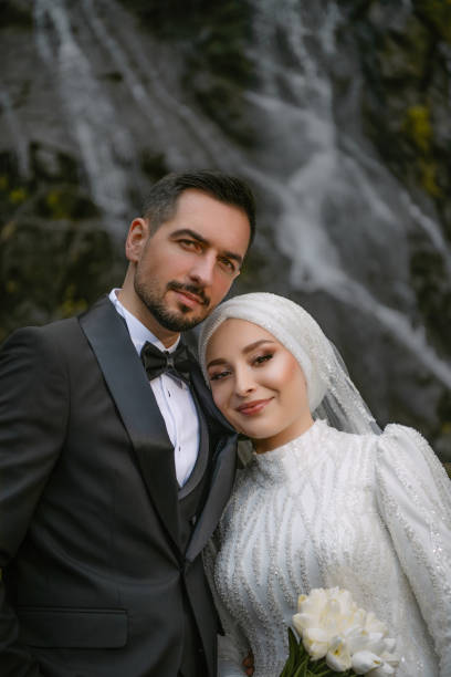 istock The bride and groom standing in front of a waterfall looking at camera smiling and posing outdoors. Newlywed bride and groom celebrating wedding 1957708649