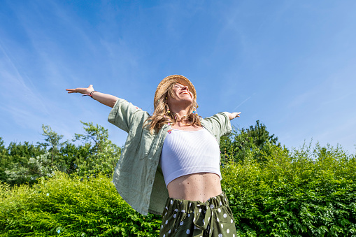 Smiling caucasian blonde woman standing with spread hands outdoors at summer day, showing freedom concept