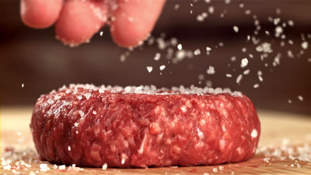The cook sprinkles salt on the meat burger. Filmed on a high-speed camera at 1000 fps.