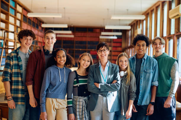 istock Happy high school teacher and her students in a library looking at camera. 1957777340