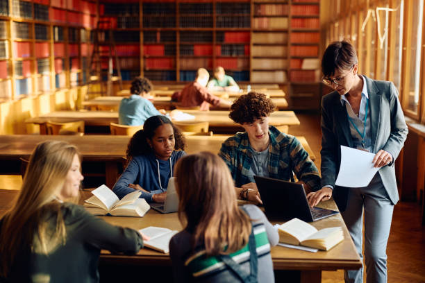 istock High school teacher using laptop with her students in a library. 1957778426