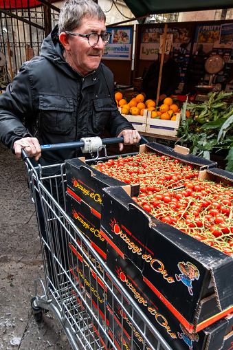Palermo, Sicily, Italy Jan 12, 2024 A man i the Mercato di Ballaro open air market uses a supermarket cart to transport tomatoes.