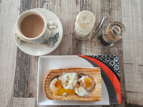 Toasted bread topped with half boiled eggs, complete with cup of coffee