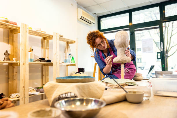 Woman working in pottery studio workshop sculpting human head.