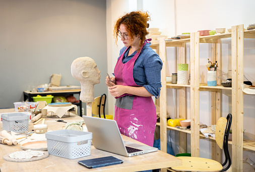 Woman working in pottery studio workshop sculpting human head.