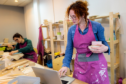Female business owner using laptop in pottery studio workshop.