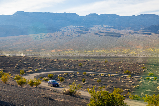 Journey through Ubehebe Crater: Solitary car kicks up dust on a winding desert road, surrounded by the rugged volcanic field and scattered bushes, creating a captivating scene of exploration