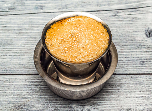 filter coffee served in steel cup isolated on wooden table top view of indian hot drink