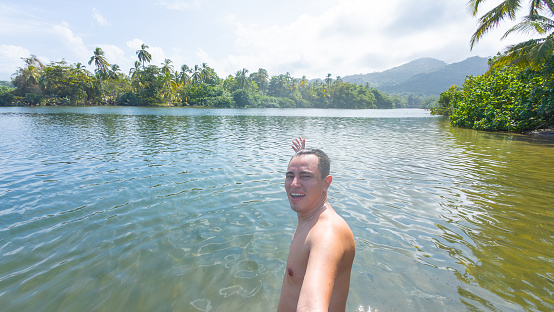 Smiling man in a natural river with tropical foliage and mountains in the background.
