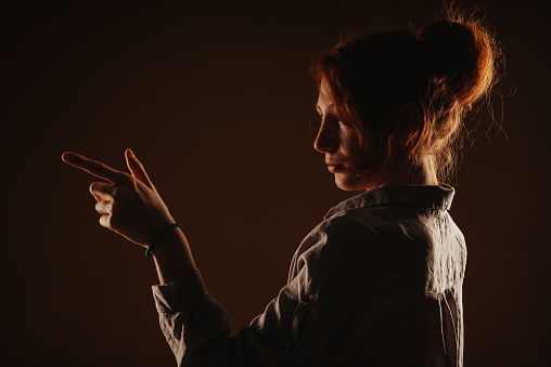 Close up of a silhouette of a ginger girl posing and pointing with her hand while standing at the studio