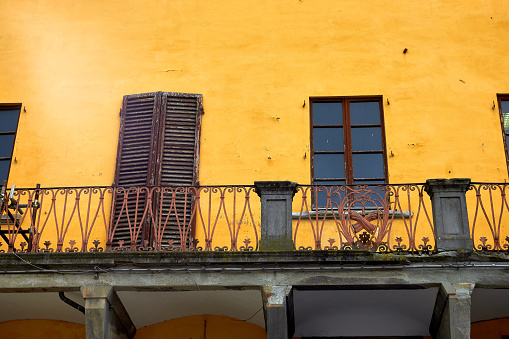 Facade of house with yellow wall, windows with brown shutters and balcony in Firenze, Italy.