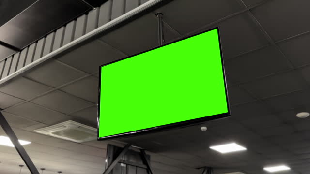 Chromakey green screen on a flat-screen TV, ceiling-mounted in a gym for dynamic content display.