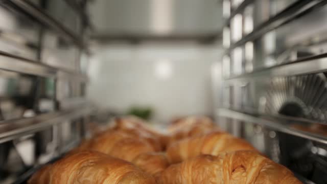 Freshly baked croissants on metallic shelves, close-up, elevator shot