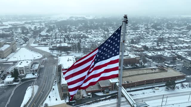 Aerial close up of American flag waving over snowy suburban landscape. Small town USA theme.