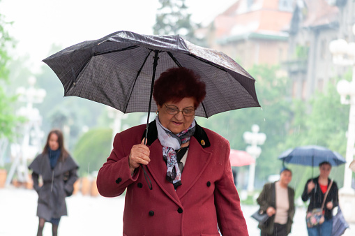 Timisoara, Romania - May 03, 2016: Woman walking on the street in the rain with an umbrella in hand. Real people.