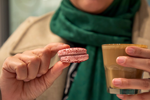 A woman drinking coffee with a macaron in a cafe