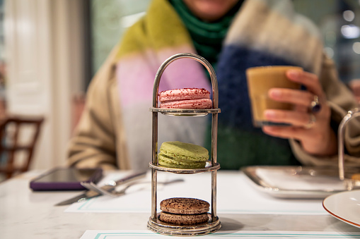 A woman drinking coffee with macarons in a cafe