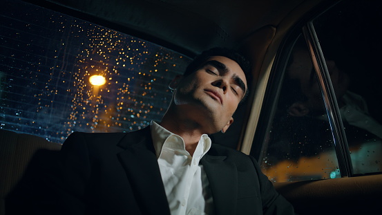 Sleeping man relaxing rainy window car close up. Formal suit tired businessman napping alone driving home at taxi. Handsome entrepreneur feeling exhausted having rest in back seat of modern automobile