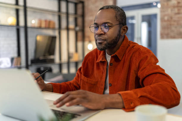 istock Dark-skinned man in red shirt working at home and looking involved 1958115785