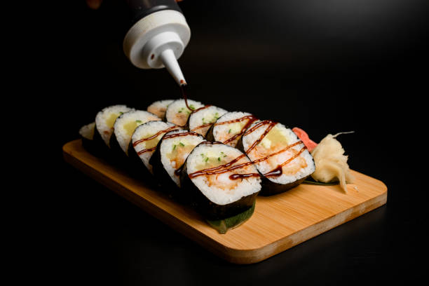 istock Sushi rolls on a wooden board are covered with sauce 1958131674