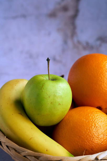 Closeup of tasty green apple with oranges and a banana inside a wicker basket.