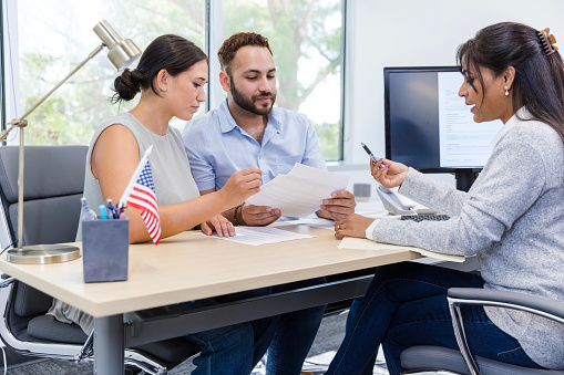 The mid adult female banker explains the loan paperwork to the young adult husband and wife.